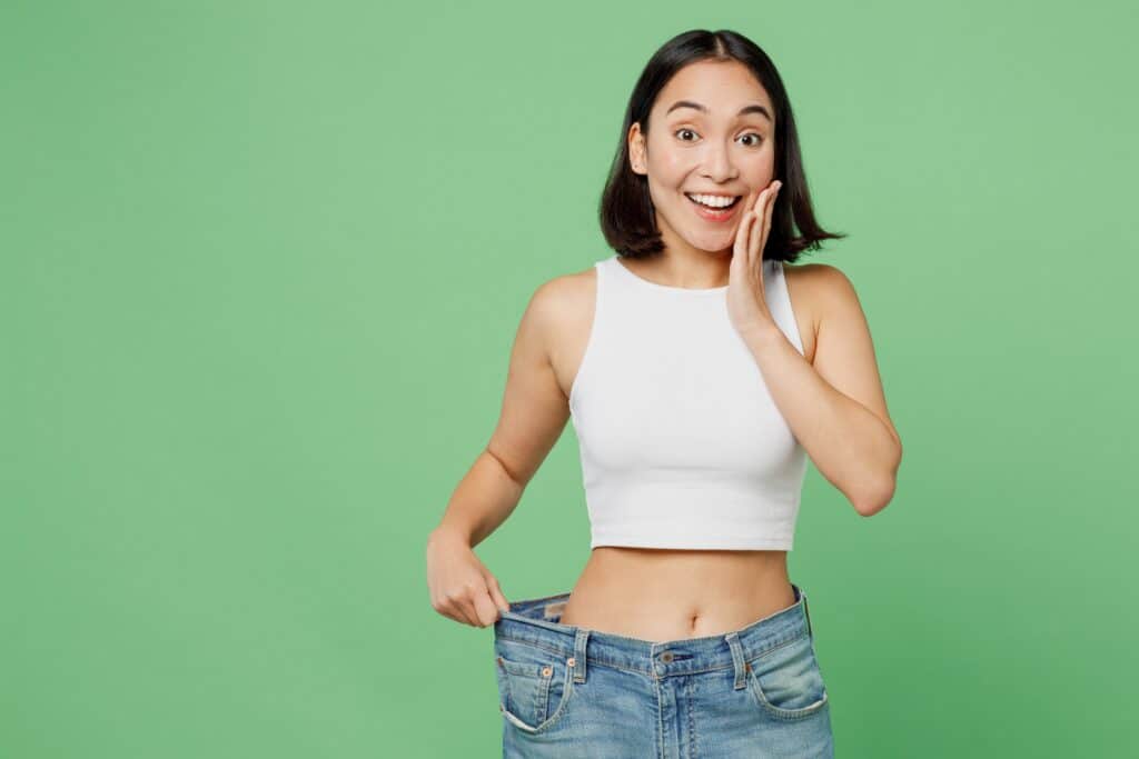 Young woman holds her too-large jeans open, revealing dramatic weight loss after taking GLP-1s for weight loss
