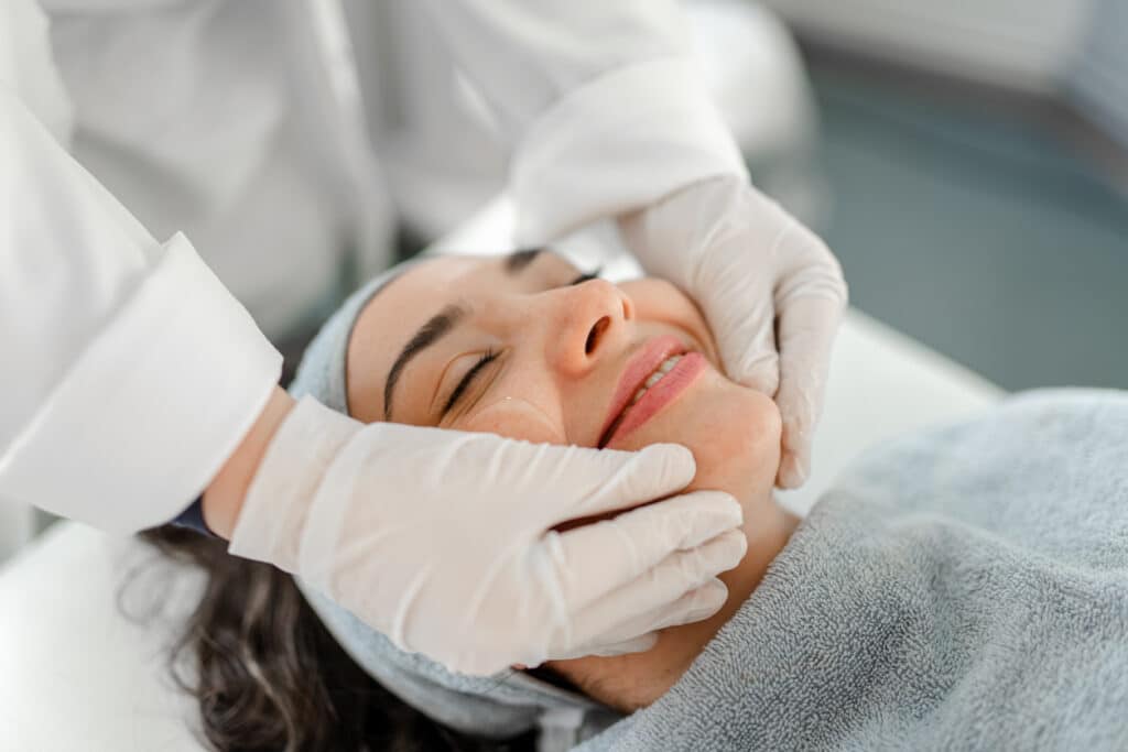Skincare provider wearing gloves gently examines a woman’s face during a post-microneedling skin assessment.